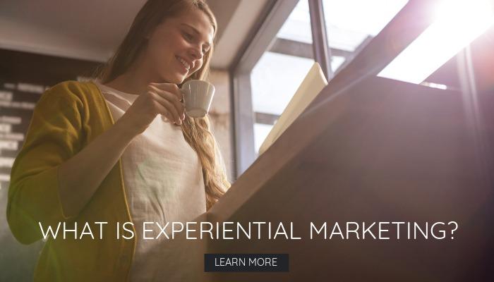 Smiling young woman with a cup of coffee working at her desk - Experiential marketing, a close look at a rising trend:  definition, examples, & ideas - Image